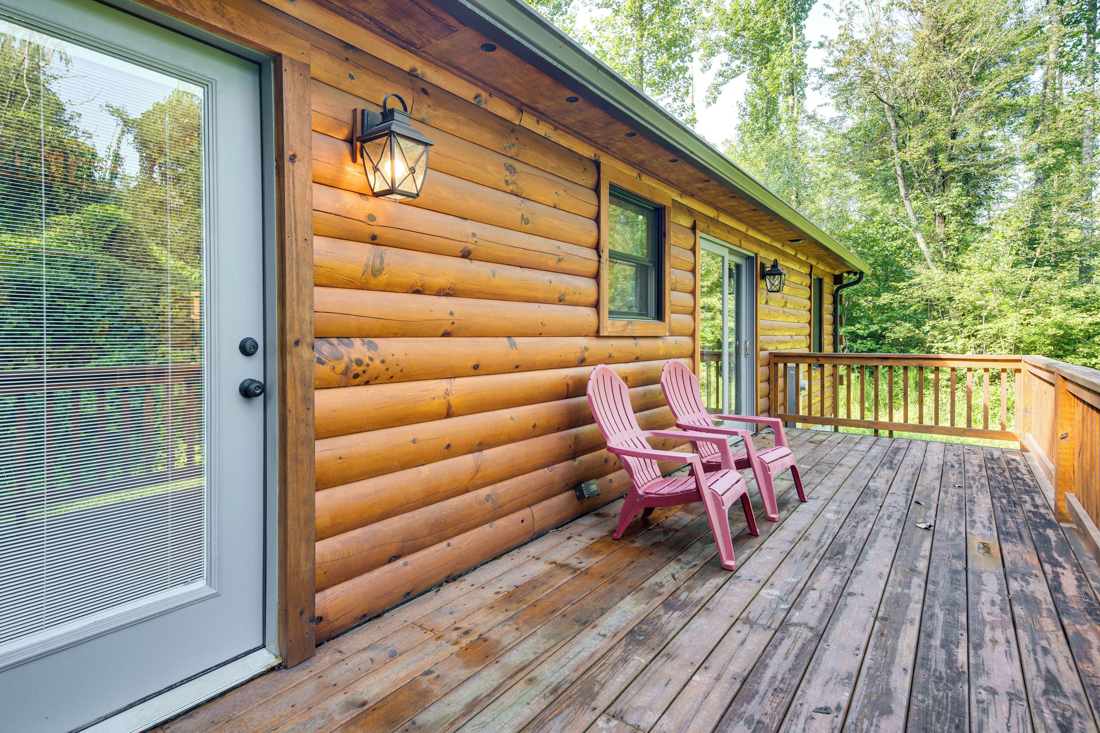 A wooden cabin with a deck, two pink Adirondack chairs, and a window with blinds.