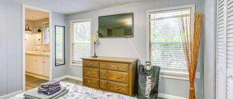 A bedroom with a bed, dresser, mirror, and windows.