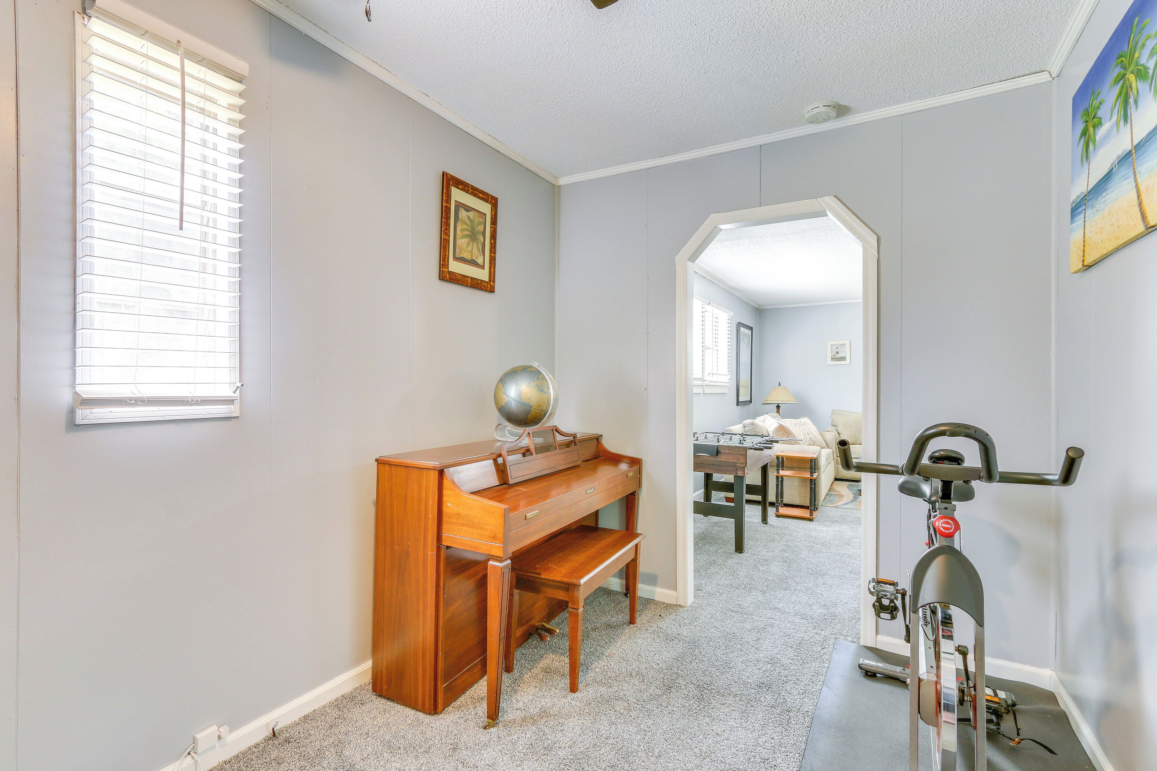 A room with a wooden desk, a globe, a bicycle, and a painting of a beach.