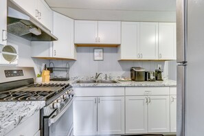 Une cuisine avec des meubles blancs, une cuisinière, un évier et un plan de travail sur lequel se trouvent divers appareils électroménagers.