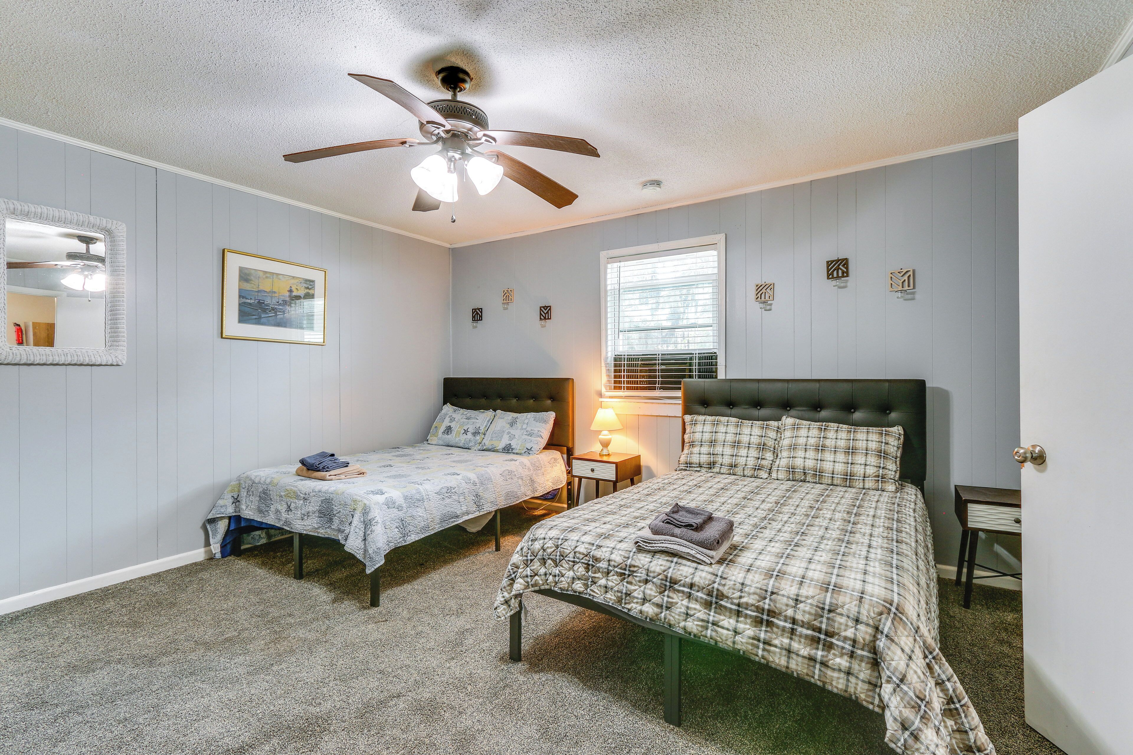 A bedroom with two single beds, a ceiling fan, a window with blinds, and a bedside table with a lamp.