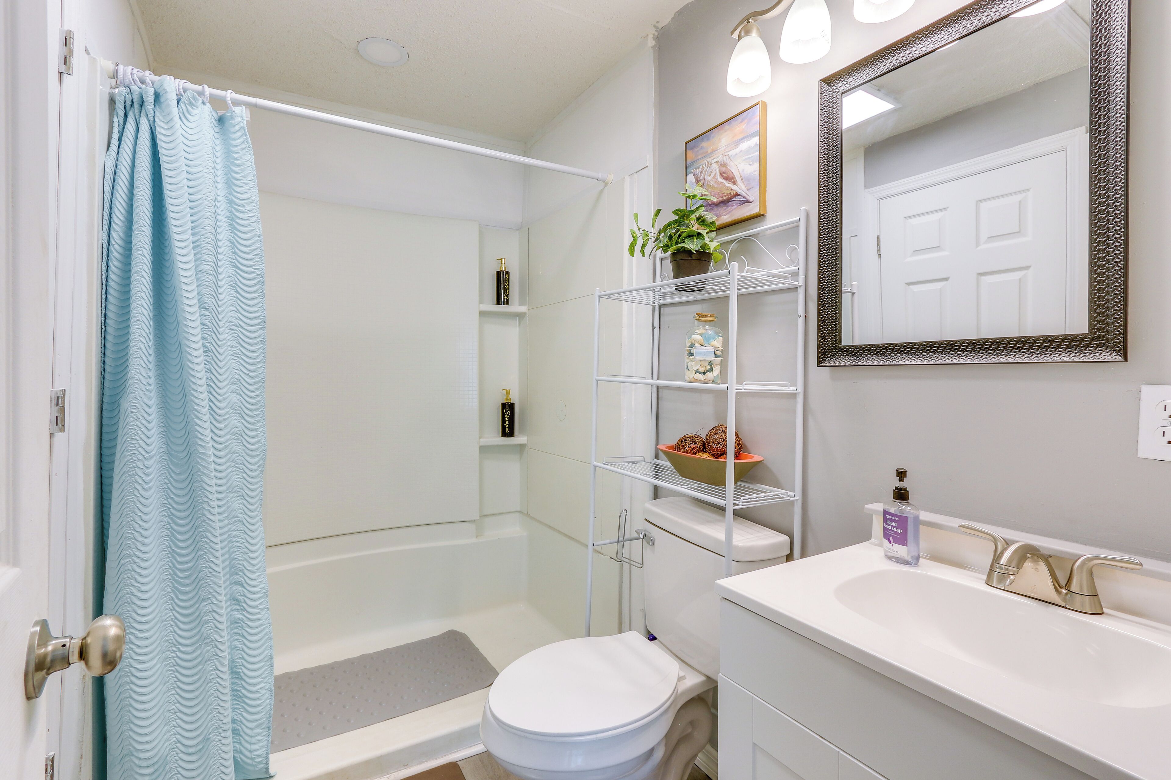 Une salle de bain équipée d’une douche, de toilettes, d’un lavabo et d’étagères où sont rangés les produits de toilette.
