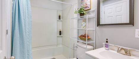 Une salle de bain équipée d’une douche, de toilettes, d’un lavabo et d’étagères où sont rangés les produits de toilette.