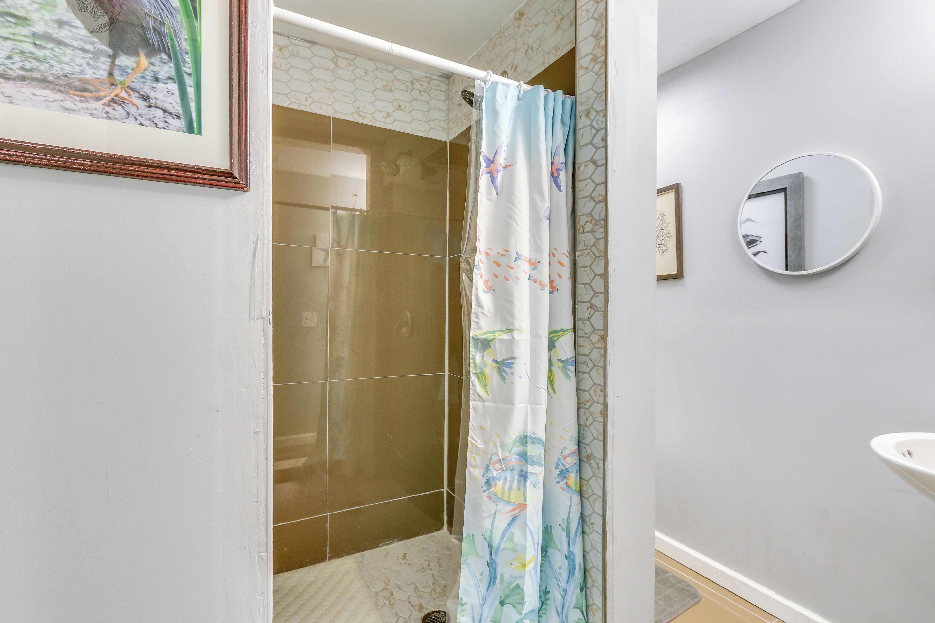 Une salle de bain avec une douche, un tableau encadré, un miroir rond et un lavabo.