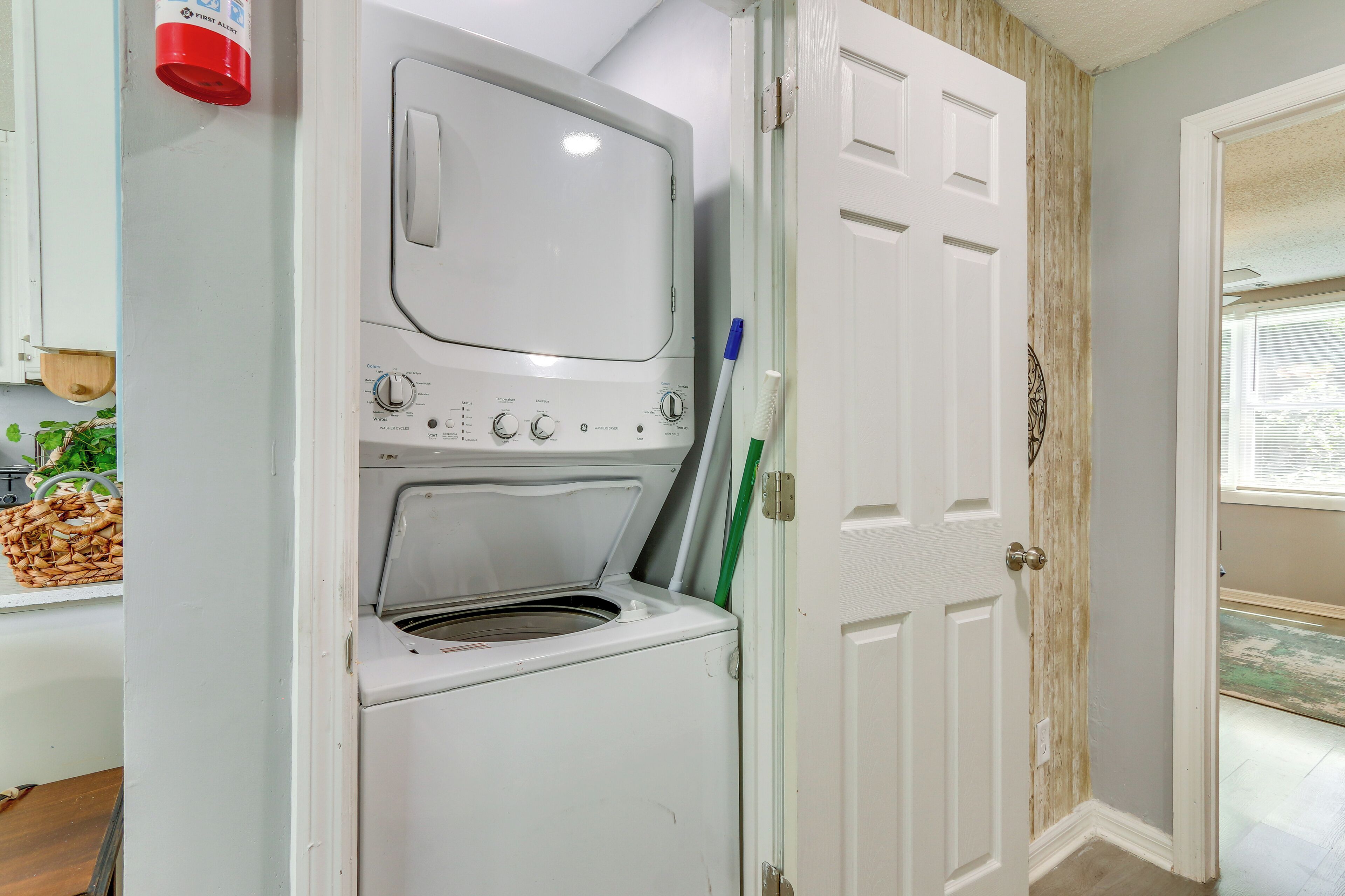 Une buanderie équipée d’un lave-linge et d’un sèche-linge à chargement frontal, d’une alarme incendie rouge et d’une porte en bois avec une fenêtre.
