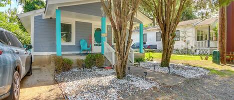 A two-story house with a porch, a car parked in the driveway, and a tree in the front yard.