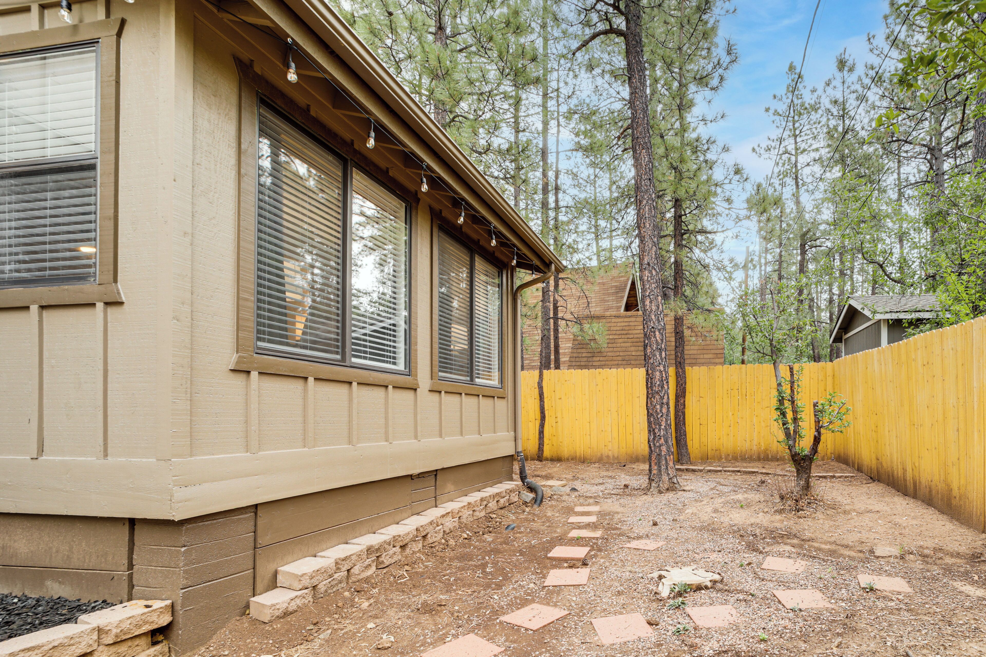 A house with a covered patio, a yellow fence, and a small tree in the yard.
