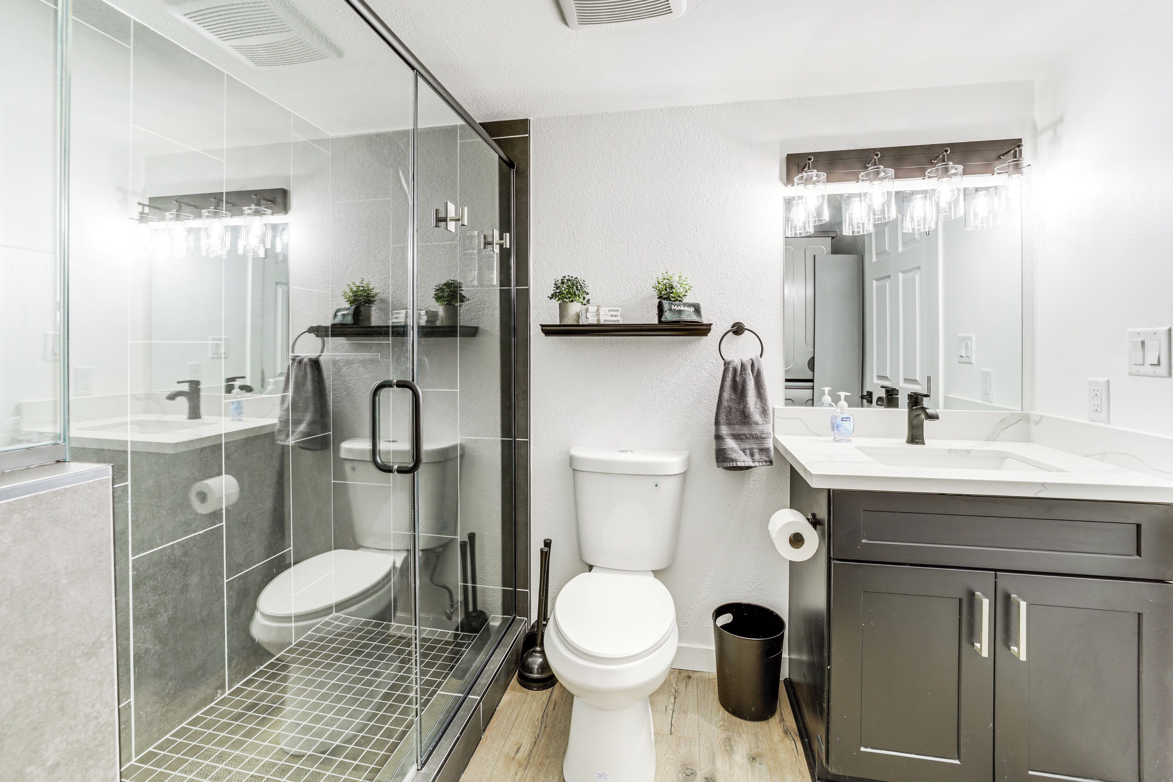 A modern bathroom with a glass shower enclosure, a toilet, a sink, and a vanity with dark cabinets.