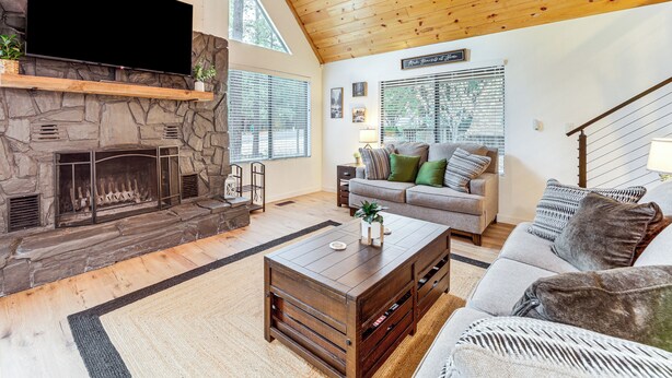 A living room with a stone fireplace, a flat-screen TV mounted above it, a wooden ceiling, a sofa with cushions, and a coffee table. - Munds Park Oasis w/ Hiking Access & Fire Pit (Munds Park)