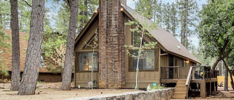 A cabin with a stone chimney, wooden deck, and a stone retaining wall.