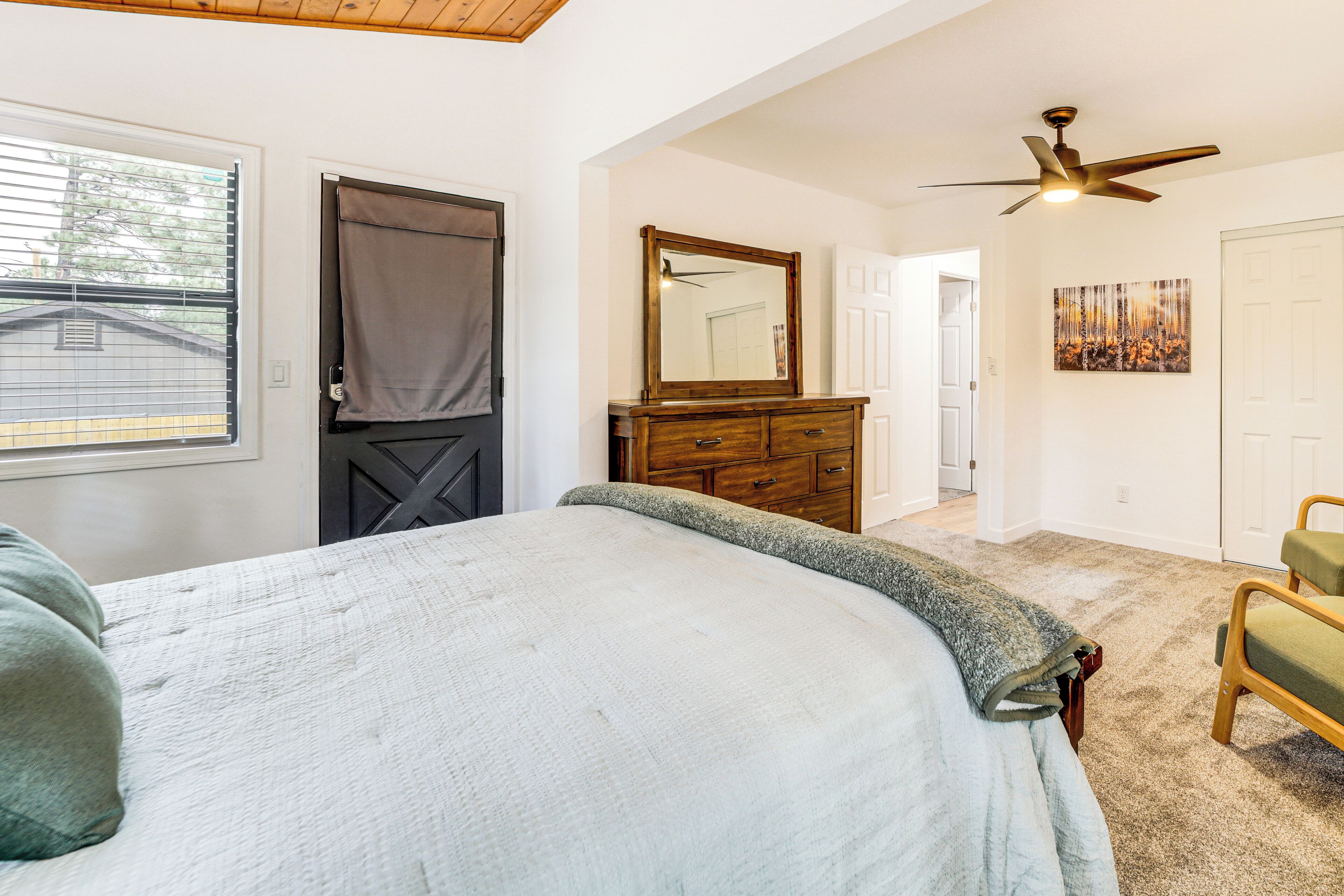 A bedroom with a bed, a dresser, a mirror, a ceiling fan, and a door leading to another room.