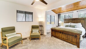 A bedroom with a wooden bed, two green armchairs, a ceiling fan, and large windows. - Munds Park Oasis w/ Hiking Access & Fire Pit (Munds Park)