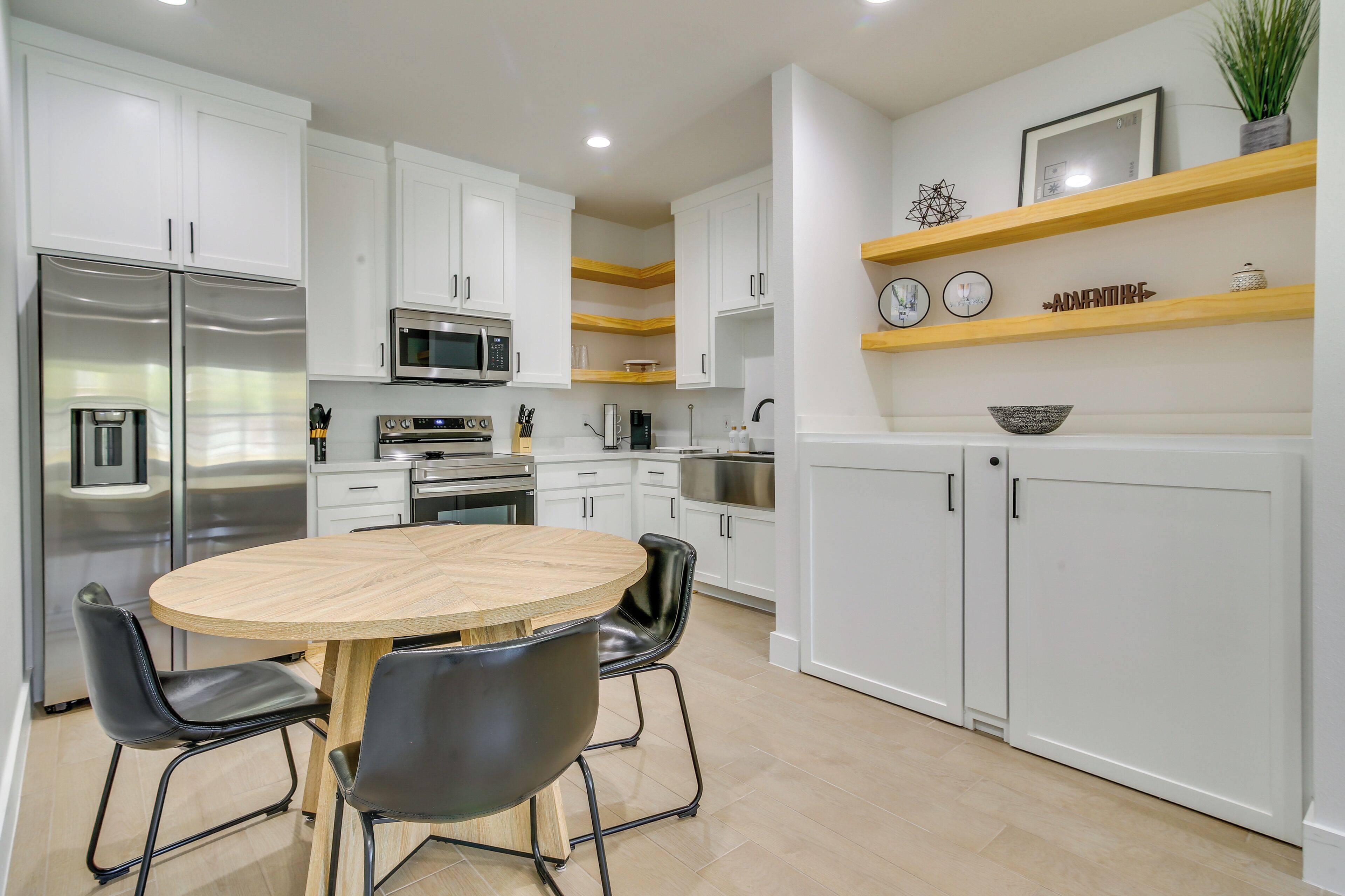 A modern kitchen with white cabinets, stainless steel appliances, a wooden dining table, and black chairs.