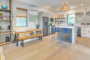 Una cocina moderna con una isla central, electrodomésticos de acero inoxidable y un comedor con mesa de madera y bancos.