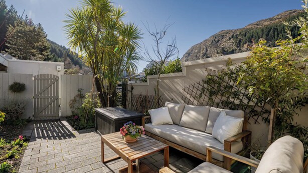 A patio with a wooden table, a sofa, and a potted plant. - Kiely Lane Lodge, Family-Friendly Queenstown Stay (Queenstown)