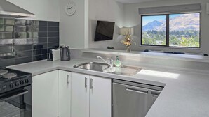 A modern kitchen with a stove, dishwasher, and a large window offering a mountain view. - Kiely Lane Lodge, Family-Friendly Queenstown Stay (Queenstown)