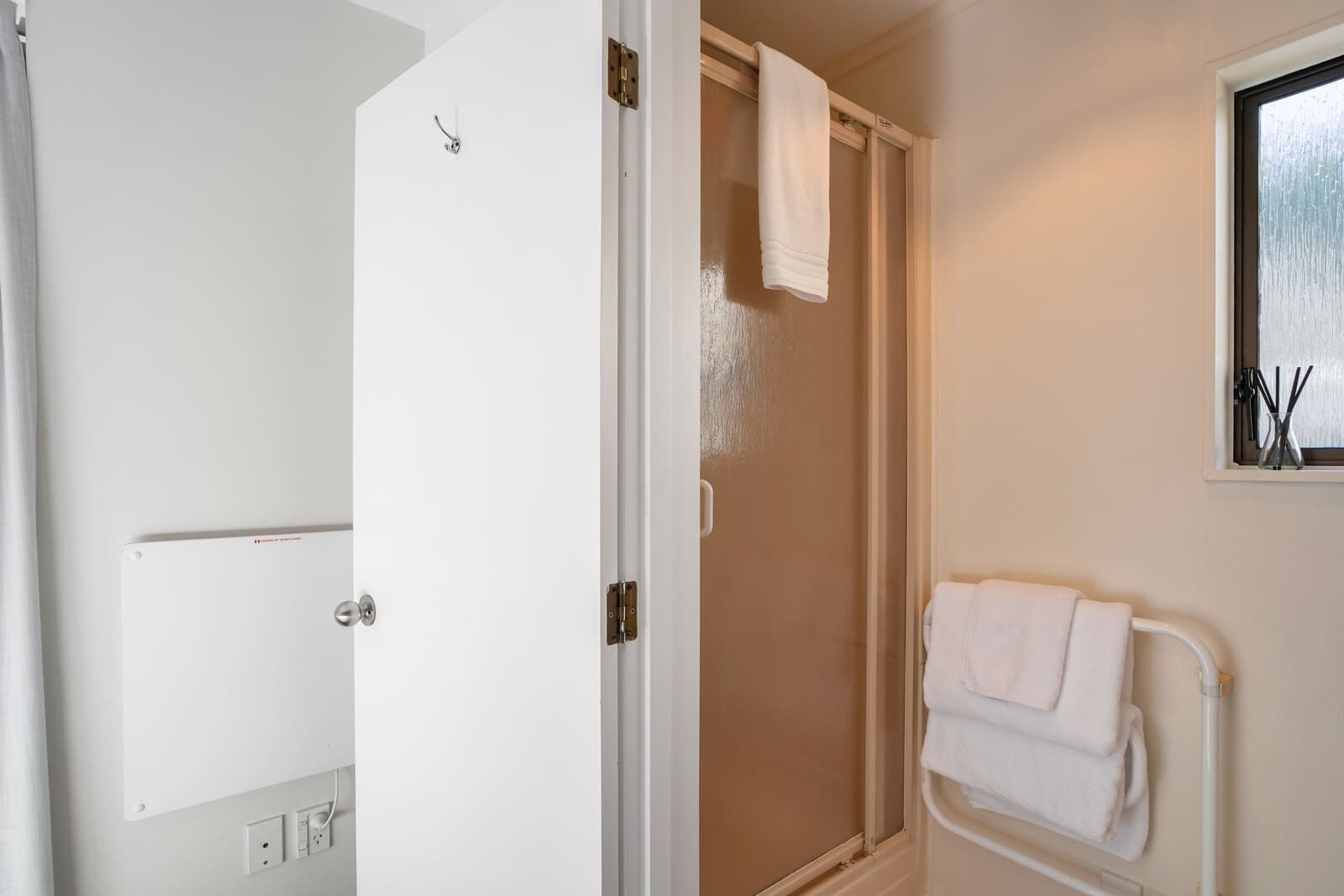 A bathroom with a shower, a towel rack, and a window with a view.