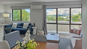 A modern living room with a sofa, a coffee table, and a view of a mountainous landscape through large windows. - Kiely Lane Lodge, Family-Friendly Queenstown Stay (Queenstown)