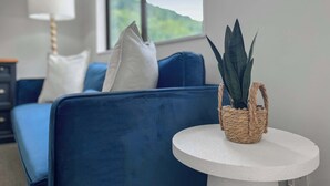 A modern living room with a blue sofa, a round white table, and a potted plant. - Kiely Lane Lodge, Family-Friendly Queenstown Stay (Queenstown)