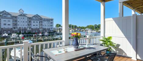 A covered outdoor area with a table and chairs, overlooking a marina with boats and a multi-story building in the background.