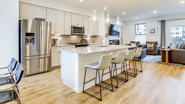 A modern kitchen with stainless steel appliances, a large island with bar stools, and a dining area with a sofa and coffee table. - Walk to Dtwn! Waterfront 3BR Cambridge Townhome (Cambridge)