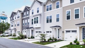 A row of townhouses with white and beige siding, front porches, and a water tower in the background. - Walk to Dtwn! Waterfront 3BR Cambridge Townhome (Cambridge)