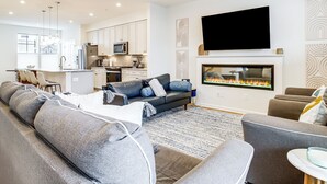 A modern living room with a grey sectional sofa, a fireplace, and a flat-screen TV mounted above it. - Walk to Dtwn! Waterfront 3BR Cambridge Townhome (Cambridge)