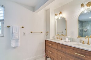 A bathroom with a large mirror, two sinks, a vanity with drawers, and a towel rack.