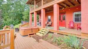 Une terrasse en bois avec un jacuzzi, des sièges d’extérieur et un escalier menant à un porche abrité.