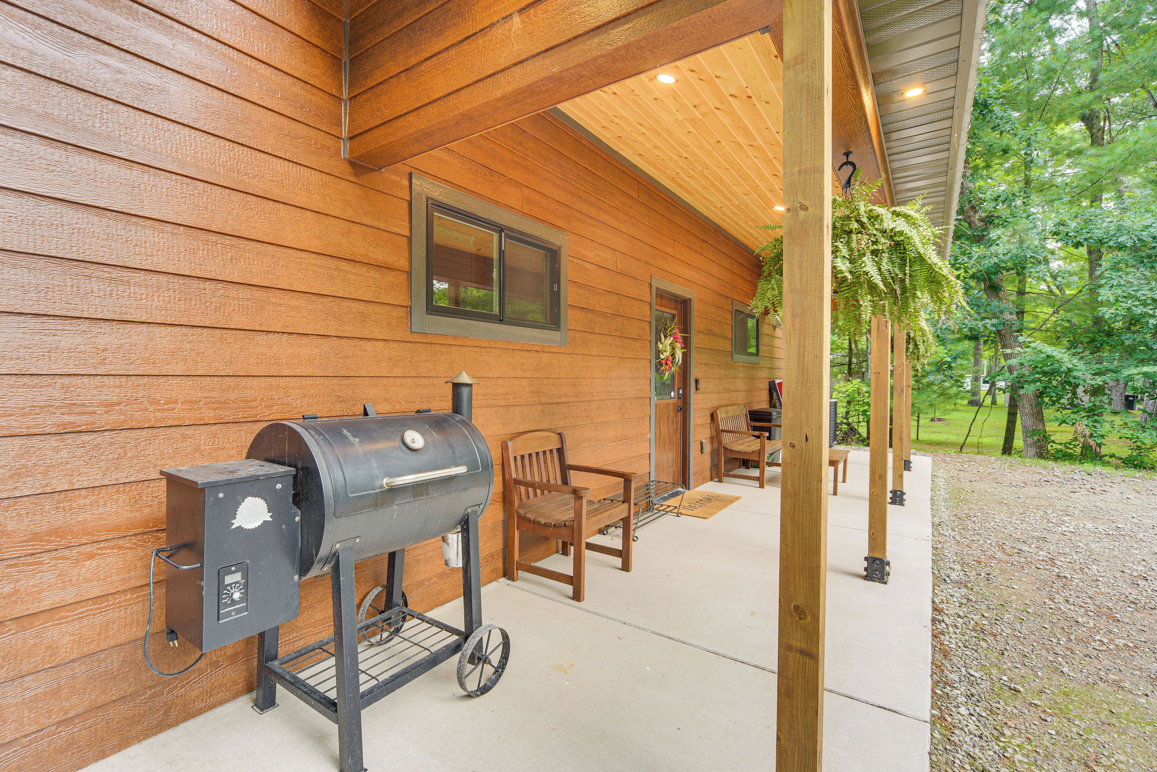 Un espacio al aire libre cubierto con una parrilla, sillas de madera y un banco.
