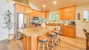 A modern kitchen with wooden cabinets, stainless steel appliances, a granite countertop, and a central island with stools. - Boat Dock, BBQ & Fireside Fun: Clam Lake Cabin (Siren)