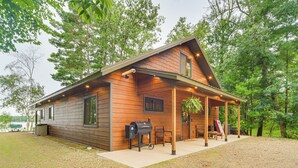 A wooden cabin with a covered porch, a barbecue grill, and a view of the surrounding forest. - Boat Dock, BBQ & Fireside Fun: Clam Lake Cabin (Siren)