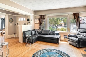 Een woonkamer met een hoekbank, een leren fauteuil, een salontafel en een kamerbreed tapijt met een patroon.