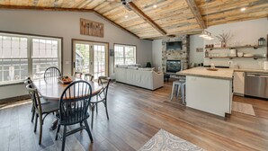 Une cuisine spacieuse avec une cheminée en pierre, des poutres apparentes en bois au plafond et un grand coin repas comprenant une table et des chaises en bois.