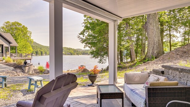 Un patio couvert avec des sièges d’extérieur, une vue sur un lac et une cheminée en pierre.