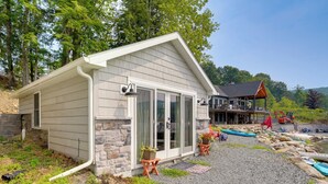 A house with a stone foundation, a garage, and a covered porch with a red roof. - Cozy Cabin on Crooked Lake: Swim, Kayak & Explore! (Averill Park)