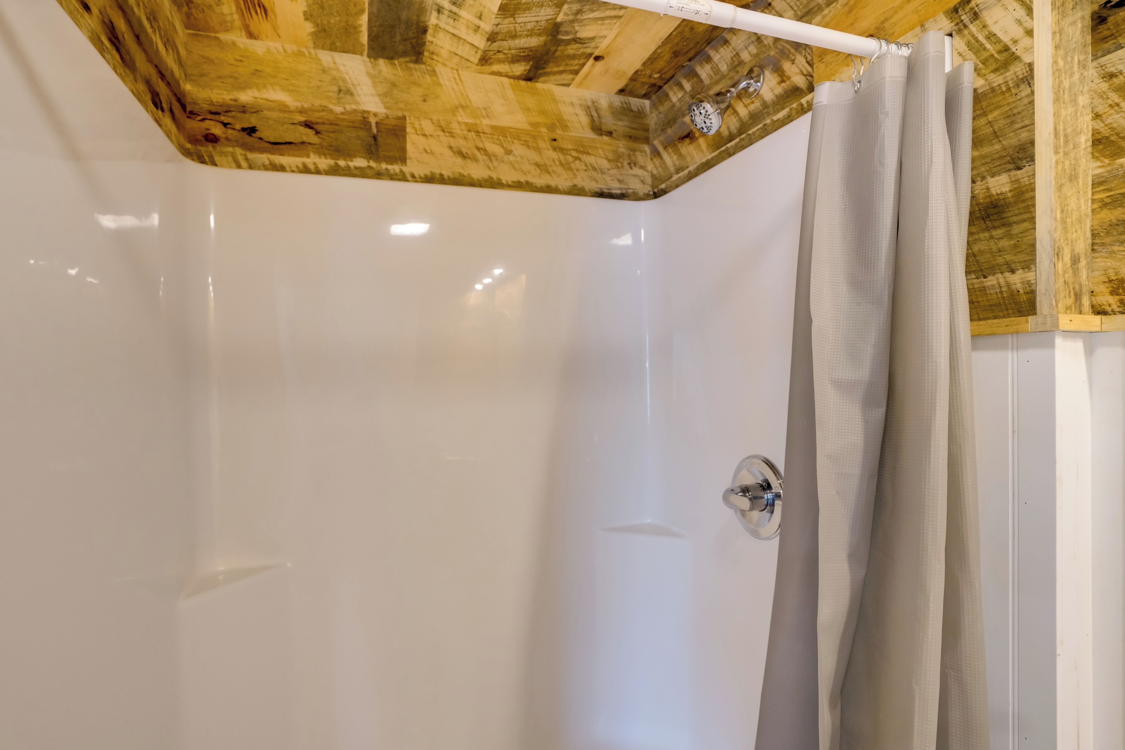 A shower area with a wooden ceiling and a white wall.