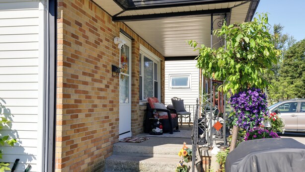 A brick house with a covered porch, steps leading to a door, and a car parked nearby. - Large Private Yard: Home 14 Mi to Niagara Falls! (Tonawanda)