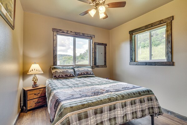 A bedroom with a bed, a nightstand, a lamp, two windows, and a ceiling fan. - Hike, Fish & Relax: Kickapoo River Cabin! (Viola)