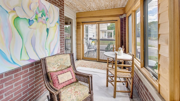 A covered patio area with a wicker chair, a table, and a large window.