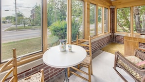A room with large windows, a round table, wicker chairs, and a brick wall.