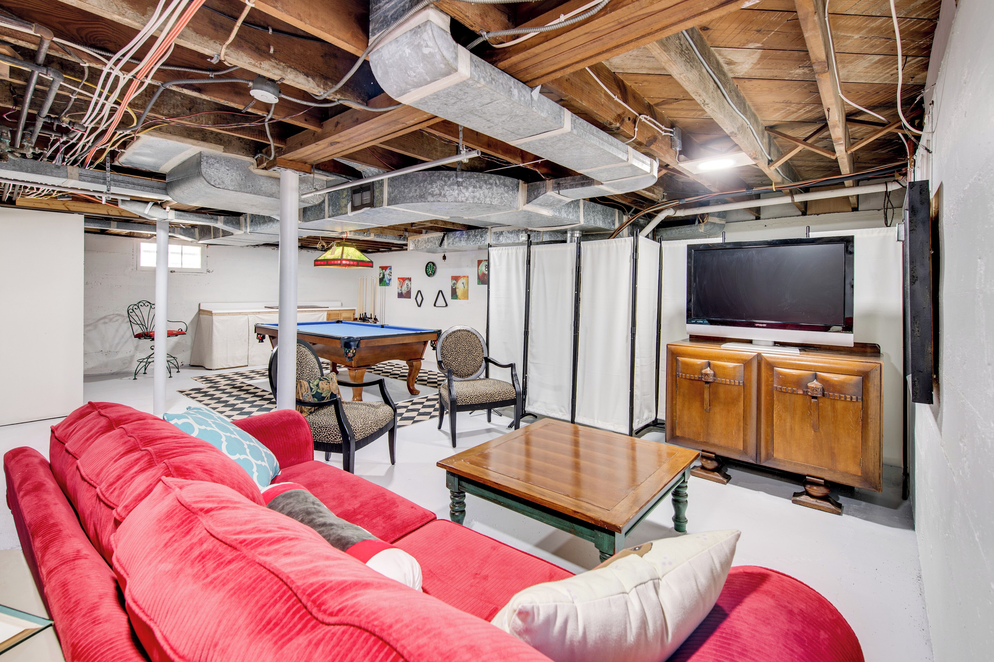 A living room with a red sofa, a wooden coffee table, a pool table, and a television on a wooden cabinet.