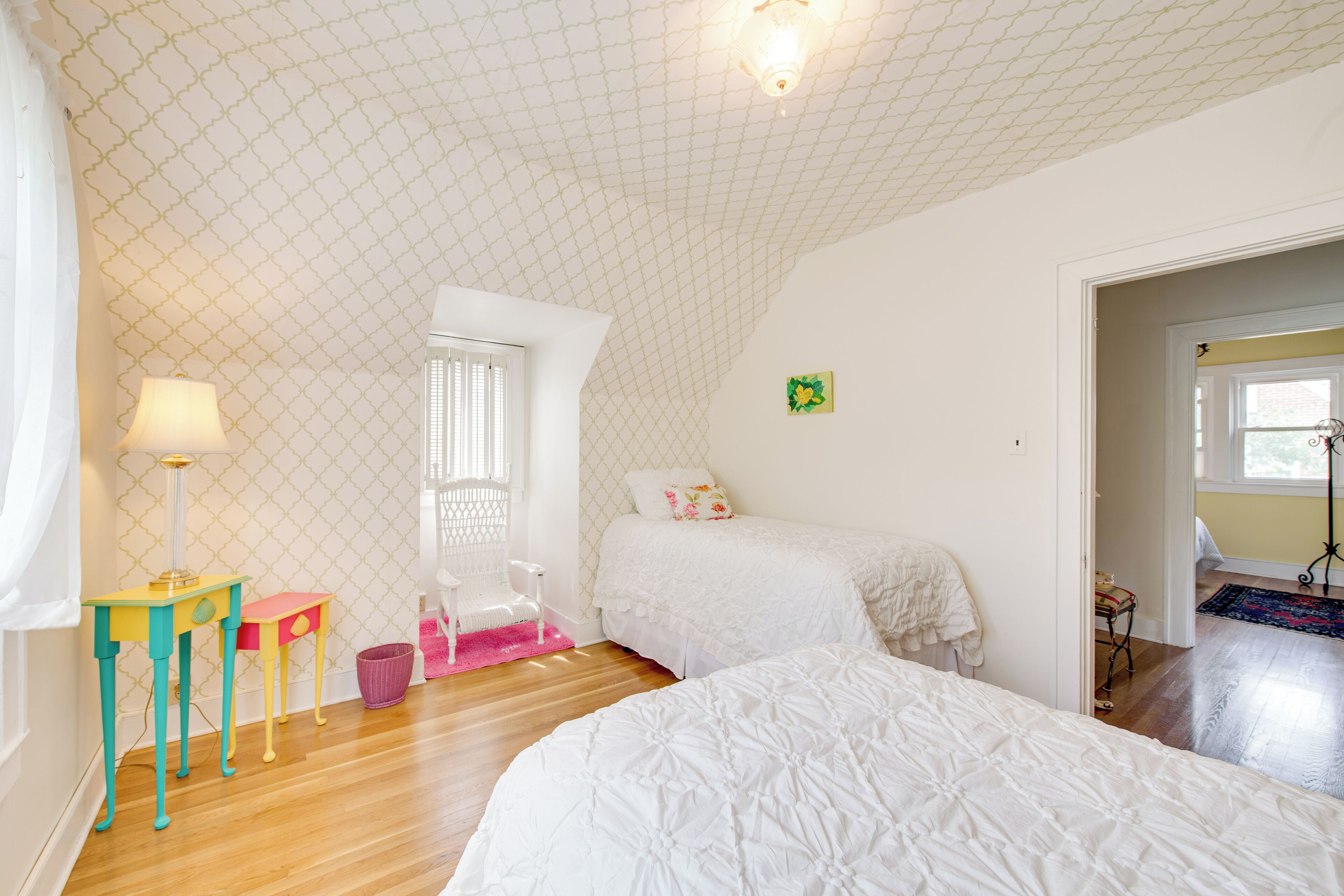 A bedroom with two beds, a window, a lamp, and a small table.