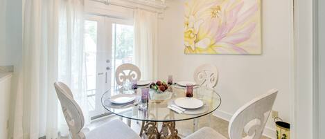 Un espace repas avec une table en verre, des chaises à revêtement blanc et un lustre.