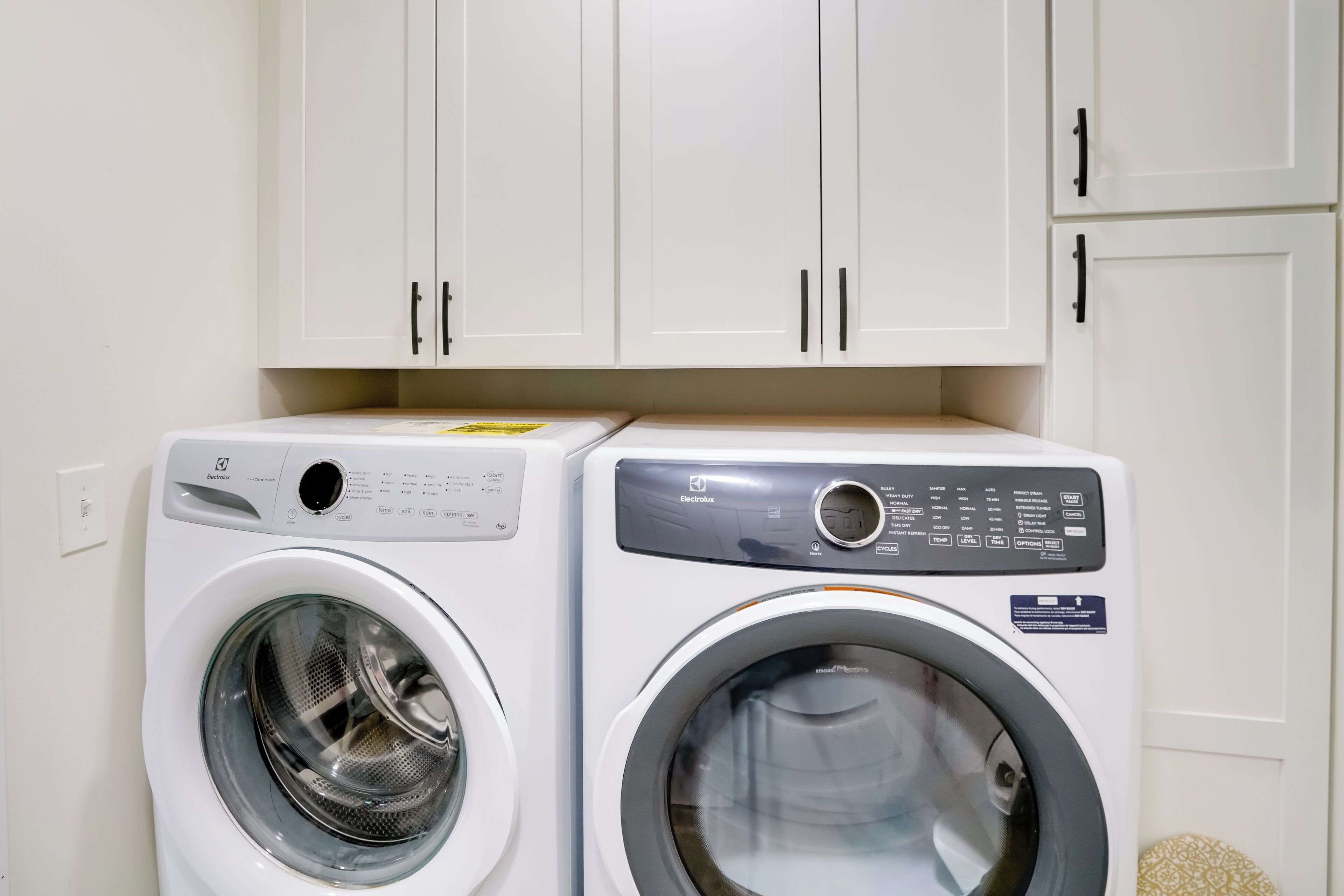Deux machines à laver à chargement frontal se trouvent dans une buanderie, au-dessus desquelles sont disposés des placards blancs.