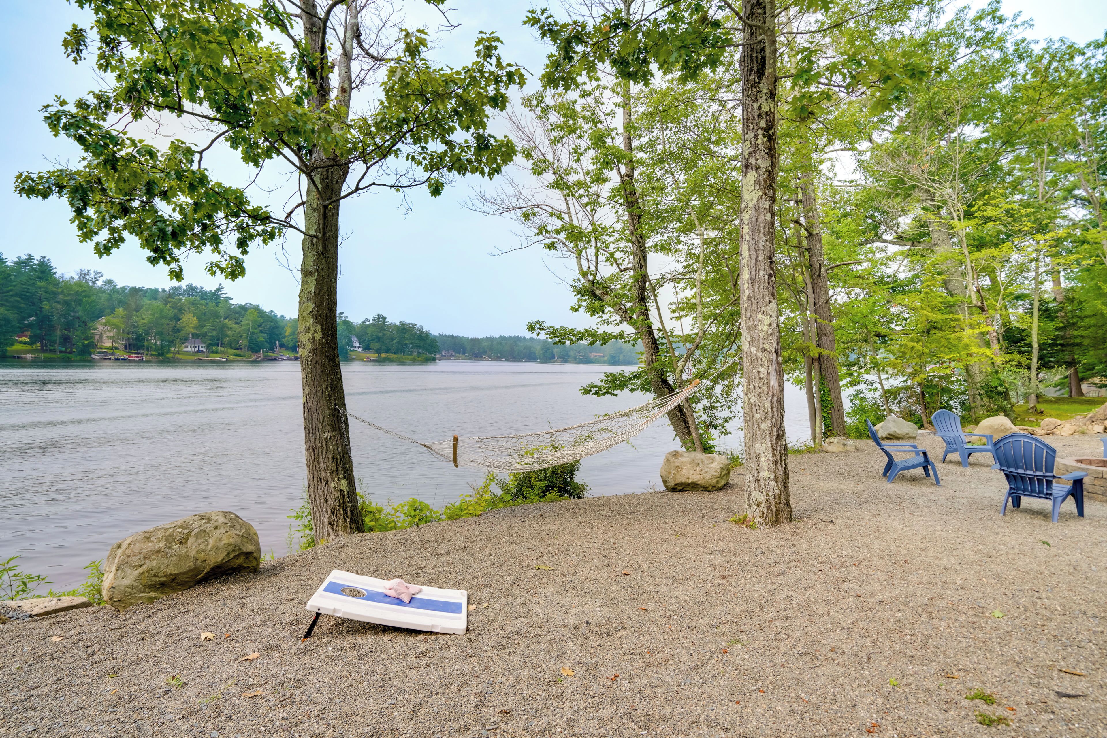 A hammock, blue Adirondack chairs, and a picnic table by a lake.