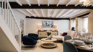 A modern living room with a round coffee table, sofas, and a dining area set for four. - Beautifully presented dog friendly - College Cottage (Burford)