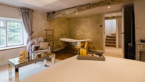A bedroom with a large bed, a glass coffee table, a chair, a sink, and a staircase leading to another room. - Beautifully presented dog friendly - College Cottage (Burford)
