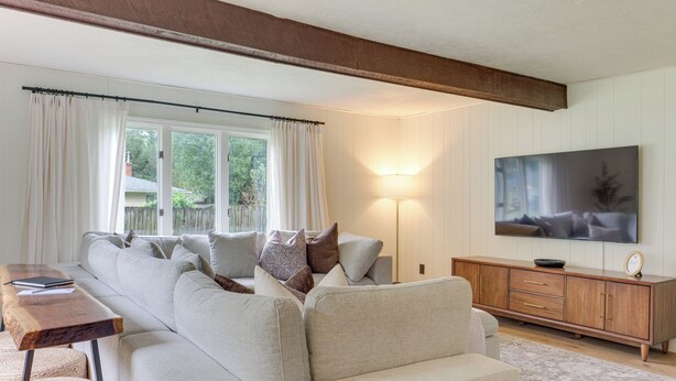 Een woonkamer met een bank, een houten salontafel, een televisie op een houten kast en een lamp.