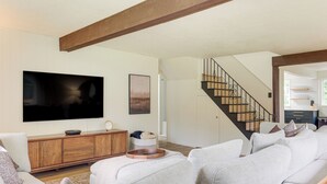 Een moderne woonkamer met een grote flatscreen-tv, een houten kast en een trap naar een bovenverdieping.